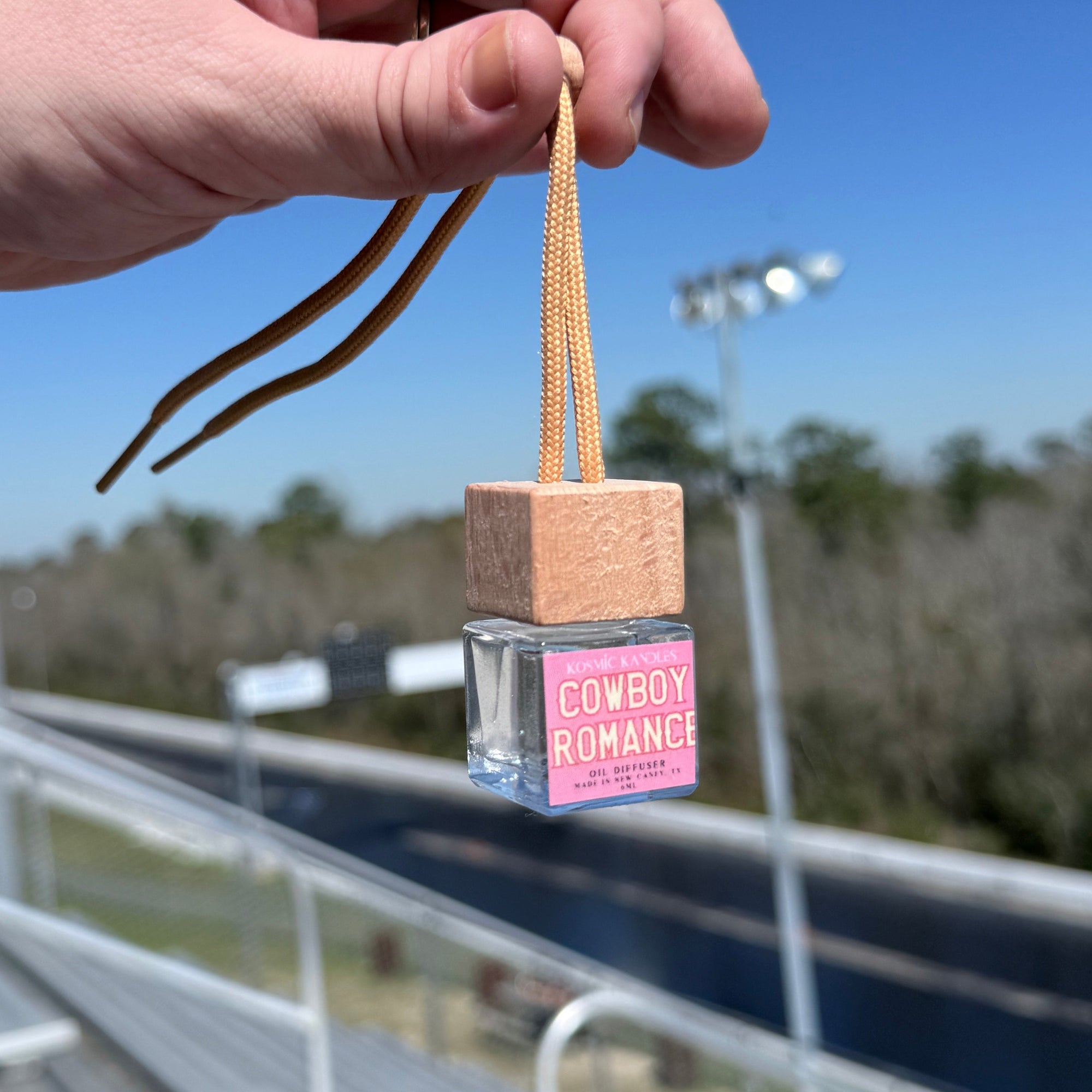 Hand holding a small bottle with a pink label against a blue sky and building background