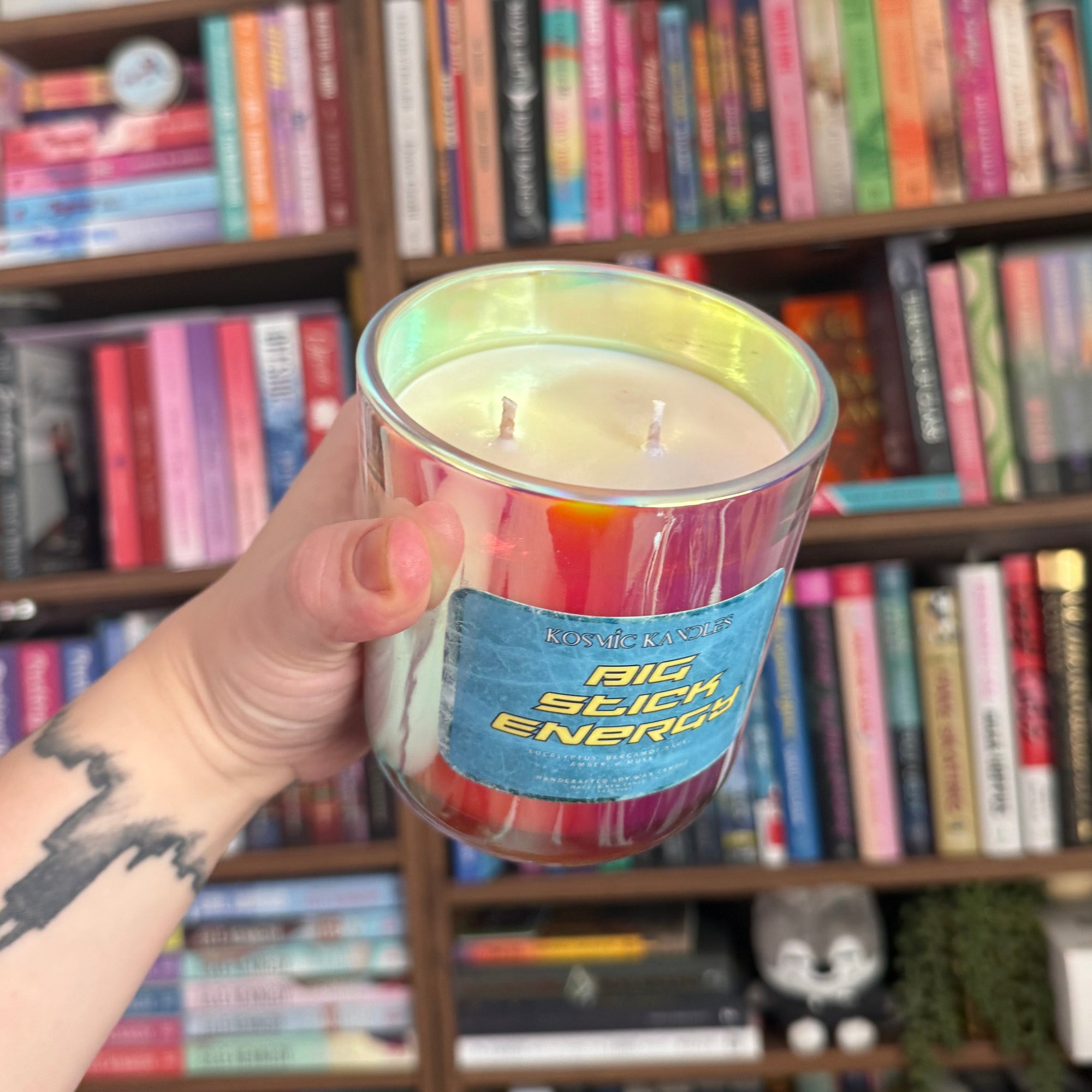 Hand holding a colorful candle in front of a bookshelf filled with books and toys