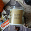 Candle Jar labeled with 'Slow Burn' on a bed of spices, tarot cards, and burnt papers